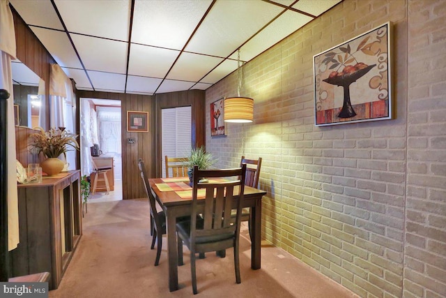 carpeted dining room featuring a drop ceiling and brick wall