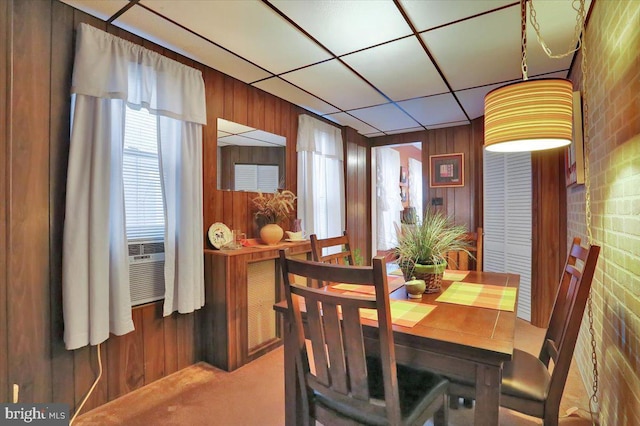 carpeted dining area with cooling unit, wooden walls, brick wall, and a drop ceiling