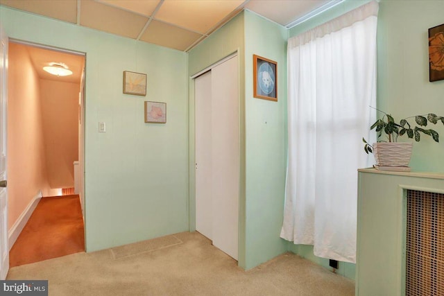 hallway with a paneled ceiling and light colored carpet