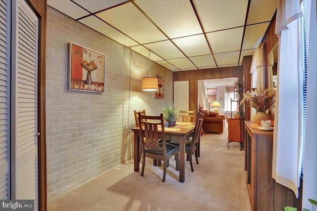 dining area with light carpet, a paneled ceiling, and brick wall