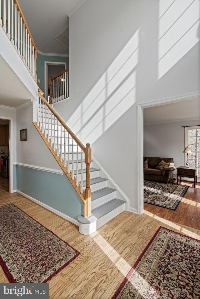 stairway featuring hardwood / wood-style floors, ornamental molding, and a high ceiling