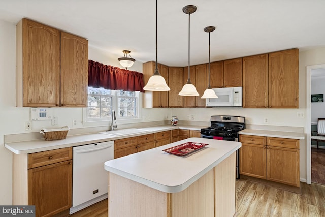 kitchen featuring sink, white appliances, a kitchen island, decorative light fixtures, and light wood-type flooring