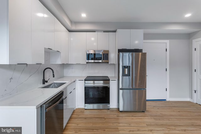 kitchen with sink, white cabinetry, light stone counters, light hardwood / wood-style flooring, and stainless steel appliances