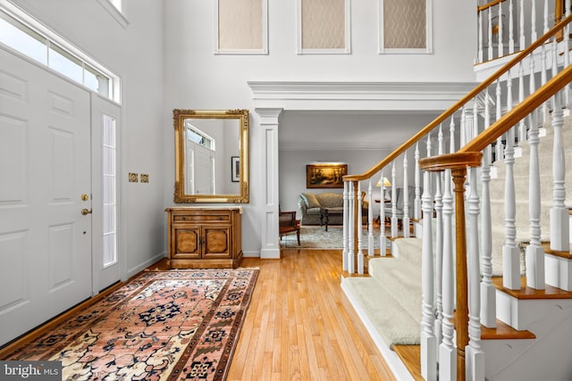 entryway featuring a towering ceiling, light wood finished floors, baseboards, and stairway