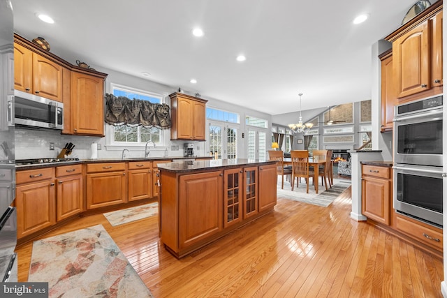 kitchen with glass insert cabinets, a notable chandelier, stainless steel appliances, light wood-type flooring, and backsplash