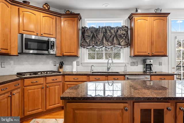 kitchen featuring appliances with stainless steel finishes, brown cabinetry, dark stone countertops, and a sink