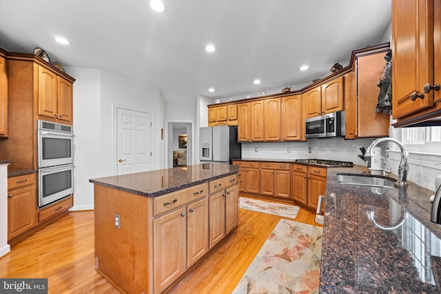 kitchen featuring stainless steel appliances, light wood finished floors, a kitchen island, and a sink