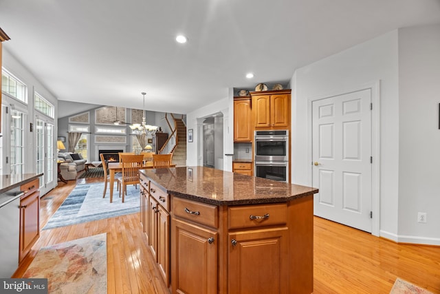 kitchen with a fireplace, light wood finished floors, double oven, a kitchen island, and dishwashing machine