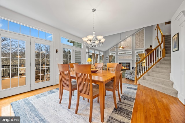 dining space with stairs, a chandelier, wood finished floors, and a glass covered fireplace