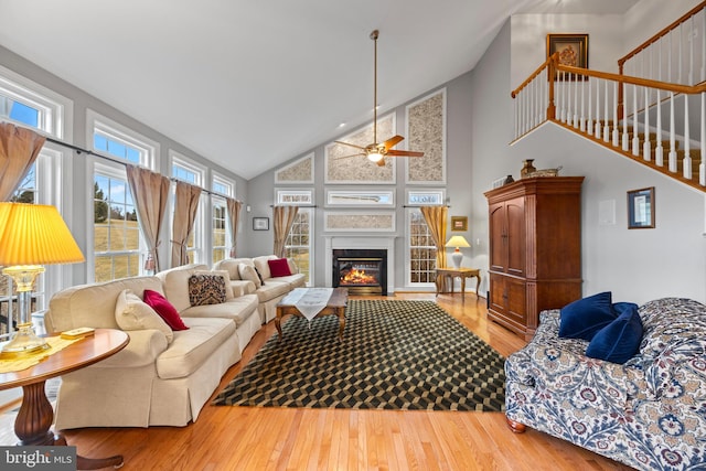 living area with high vaulted ceiling, stairway, wood finished floors, and a glass covered fireplace