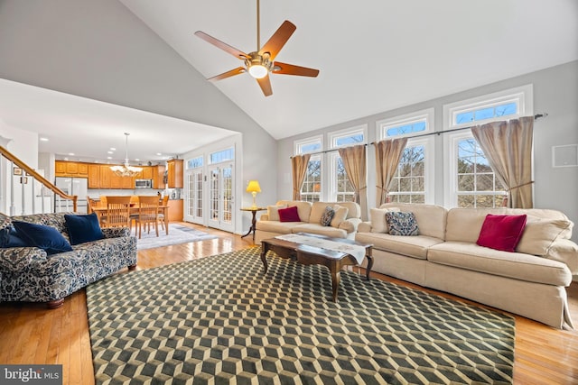 living area with ceiling fan with notable chandelier, high vaulted ceiling, light wood-type flooring, and a wealth of natural light