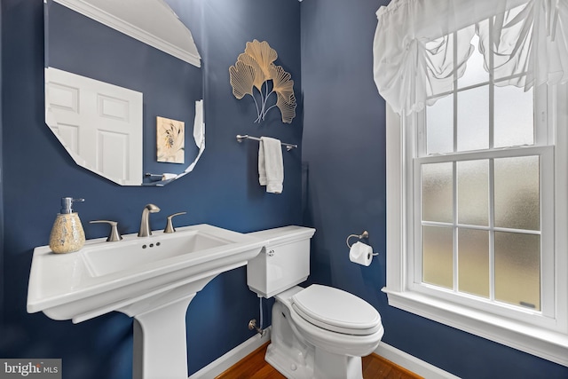 half bathroom with baseboards, toilet, and wood finished floors