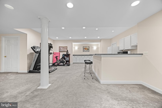 exercise area featuring baseboards, recessed lighting, decorative columns, and light colored carpet