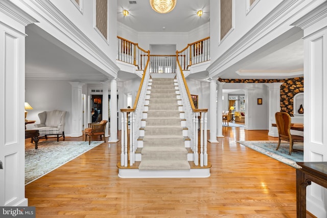 entrance foyer with ornamental molding, light wood-style flooring, and decorative columns