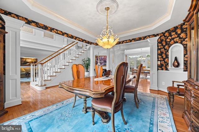 dining space with crown molding, a notable chandelier, a raised ceiling, stairway, and ornate columns