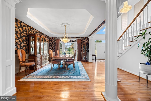 dining area featuring hardwood / wood-style floors, stairway, a tray ceiling, decorative columns, and crown molding