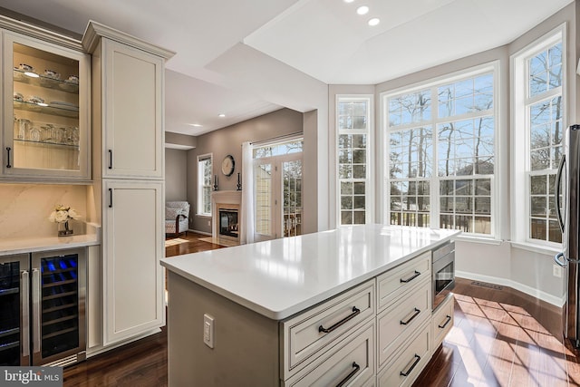 kitchen featuring a kitchen island, stainless steel microwave, beverage cooler, and dark hardwood / wood-style flooring