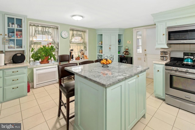 kitchen featuring a center island, light tile patterned floors, appliances with stainless steel finishes, a kitchen breakfast bar, and decorative backsplash