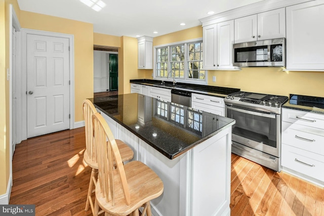 kitchen with a breakfast bar, a center island, light hardwood / wood-style flooring, appliances with stainless steel finishes, and white cabinets