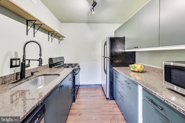 kitchen with sink, light wood-type flooring, light stone countertops, and appliances with stainless steel finishes