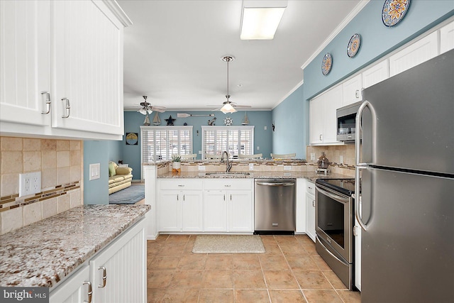 kitchen featuring ceiling fan, ornamental molding, appliances with stainless steel finishes, a peninsula, and a sink