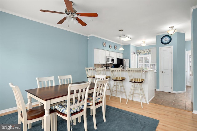 dining space featuring crown molding, a ceiling fan, baseboards, and light wood finished floors