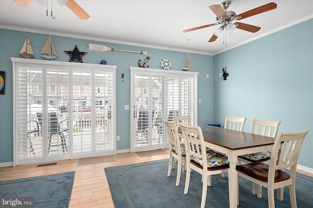 dining room featuring wood finished floors, visible vents, baseboards, ornamental molding, and ceiling fan