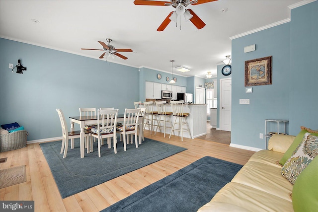 dining space with crown molding, light wood-style flooring, a ceiling fan, and baseboards