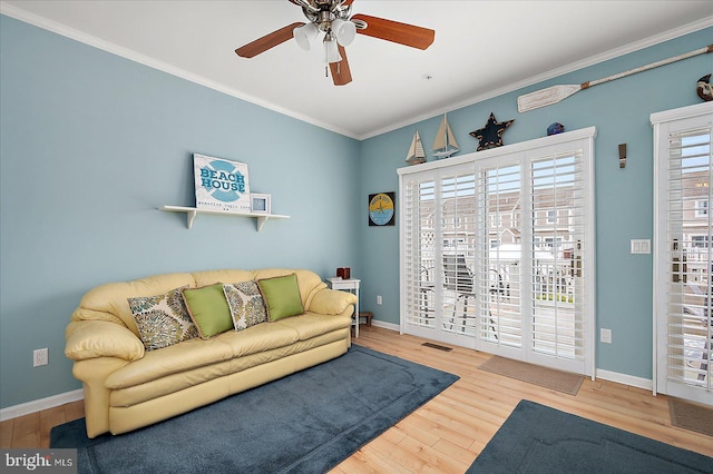 living room featuring visible vents, crown molding, baseboards, ceiling fan, and wood finished floors