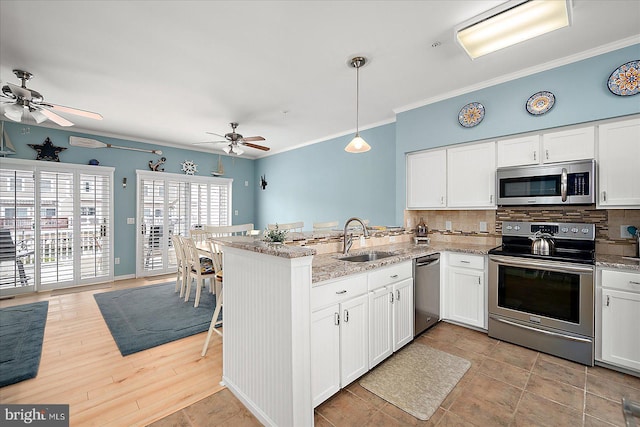 kitchen featuring a ceiling fan, a sink, tasteful backsplash, stainless steel appliances, and a peninsula