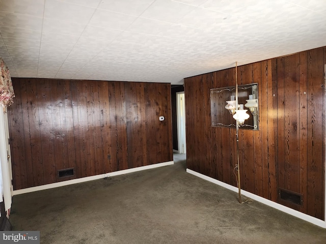 empty room with wooden walls, a chandelier, and dark colored carpet