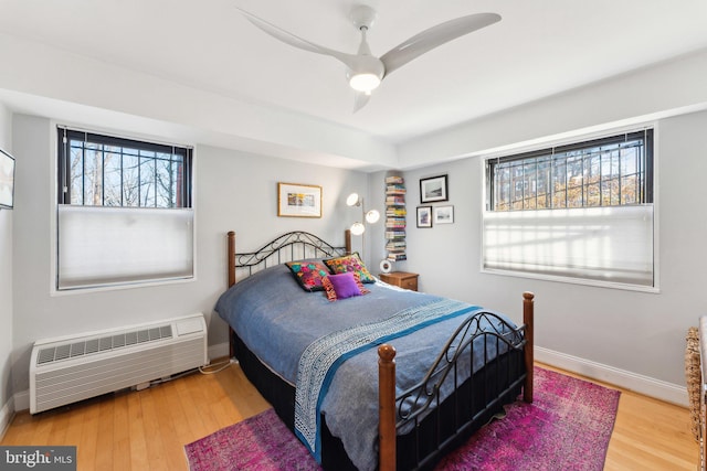 bedroom with ceiling fan, a wall mounted AC, and wood-type flooring