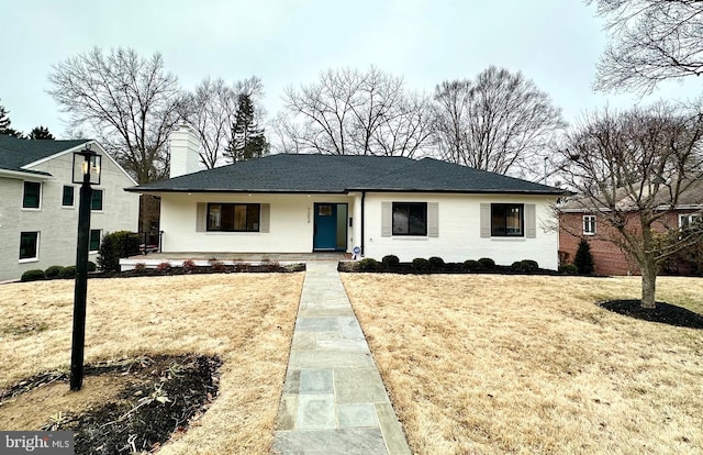 view of front of home featuring brick siding, a chimney, and a front lawn