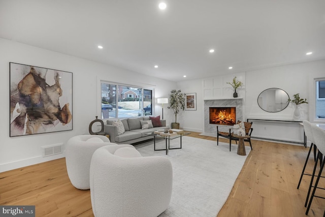 living room with recessed lighting, a high end fireplace, baseboards, visible vents, and light wood finished floors