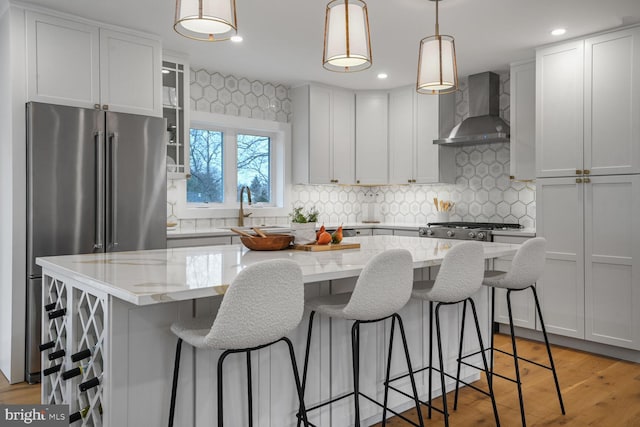 kitchen featuring high quality fridge, a kitchen island, a sink, light stone countertops, and wall chimney exhaust hood