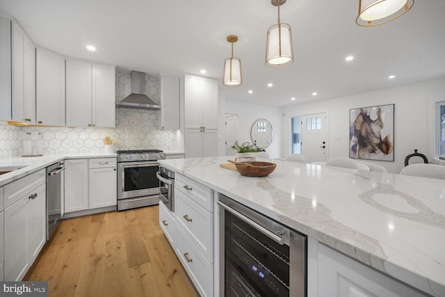 kitchen featuring wine cooler, hanging light fixtures, appliances with stainless steel finishes, white cabinets, and wall chimney range hood