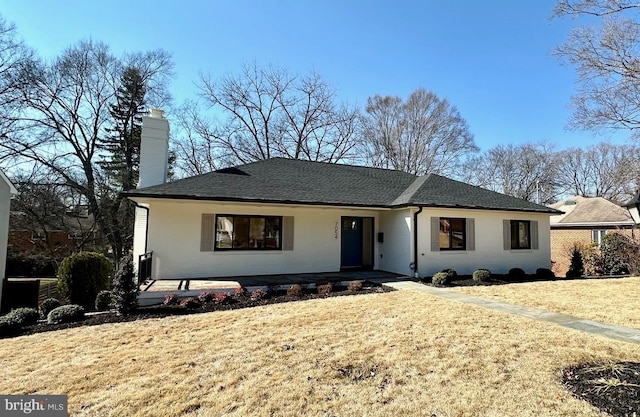 ranch-style home featuring brick siding, a chimney, a front yard, and a shingled roof