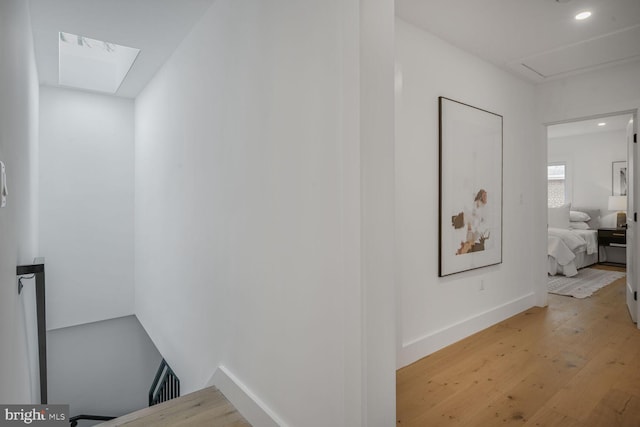 hall with light wood finished floors, baseboards, a skylight, and recessed lighting