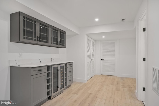 bar featuring light wood-style flooring, recessed lighting, beverage cooler, visible vents, and baseboards