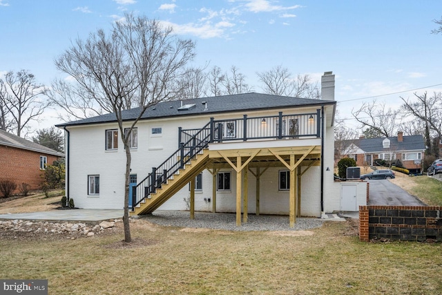 back of property with a deck, brick siding, stairs, a lawn, and a chimney