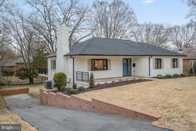 single story home featuring brick siding, a chimney, a porch, a shingled roof, and cooling unit