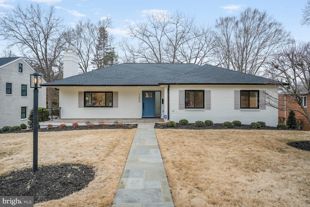 view of front of home with covered porch, brick siding, a front lawn, and a shingled roof