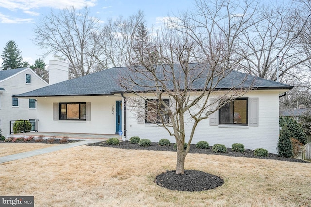 ranch-style home with a front yard, brick siding, a chimney, and roof with shingles