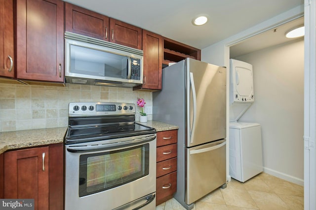 kitchen with appliances with stainless steel finishes, tasteful backsplash, stacked washer and clothes dryer, light tile patterned floors, and light stone countertops