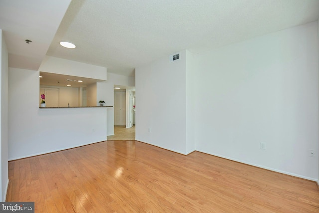 unfurnished living room with light hardwood / wood-style flooring and a textured ceiling