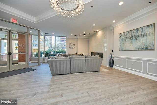 living room with a notable chandelier, crown molding, light hardwood / wood-style flooring, and french doors