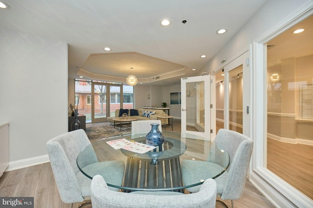 dining room featuring a tray ceiling, light wood-type flooring, and french doors