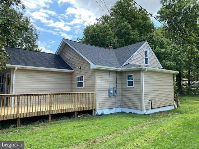 rear view of property featuring a deck, a shingled roof, and a lawn