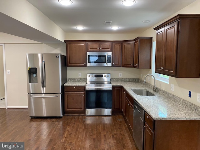 kitchen with stainless steel appliances, a sink, visible vents, light stone countertops, and dark wood-style floors