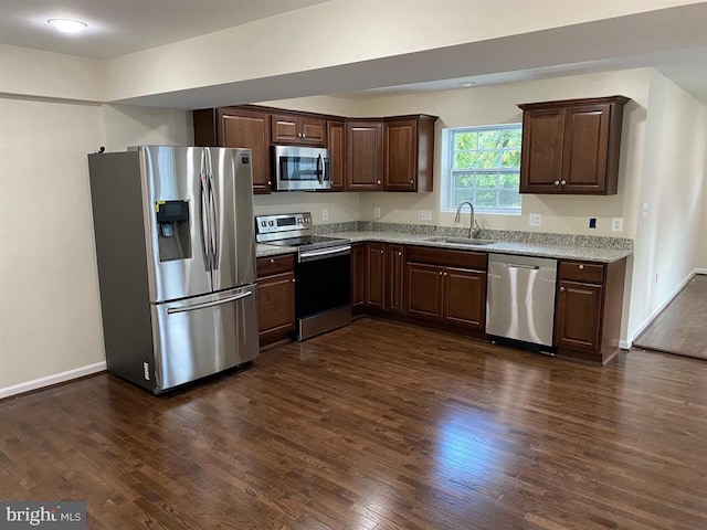 kitchen featuring dark wood-style flooring, appliances with stainless steel finishes, dark brown cabinetry, a sink, and baseboards